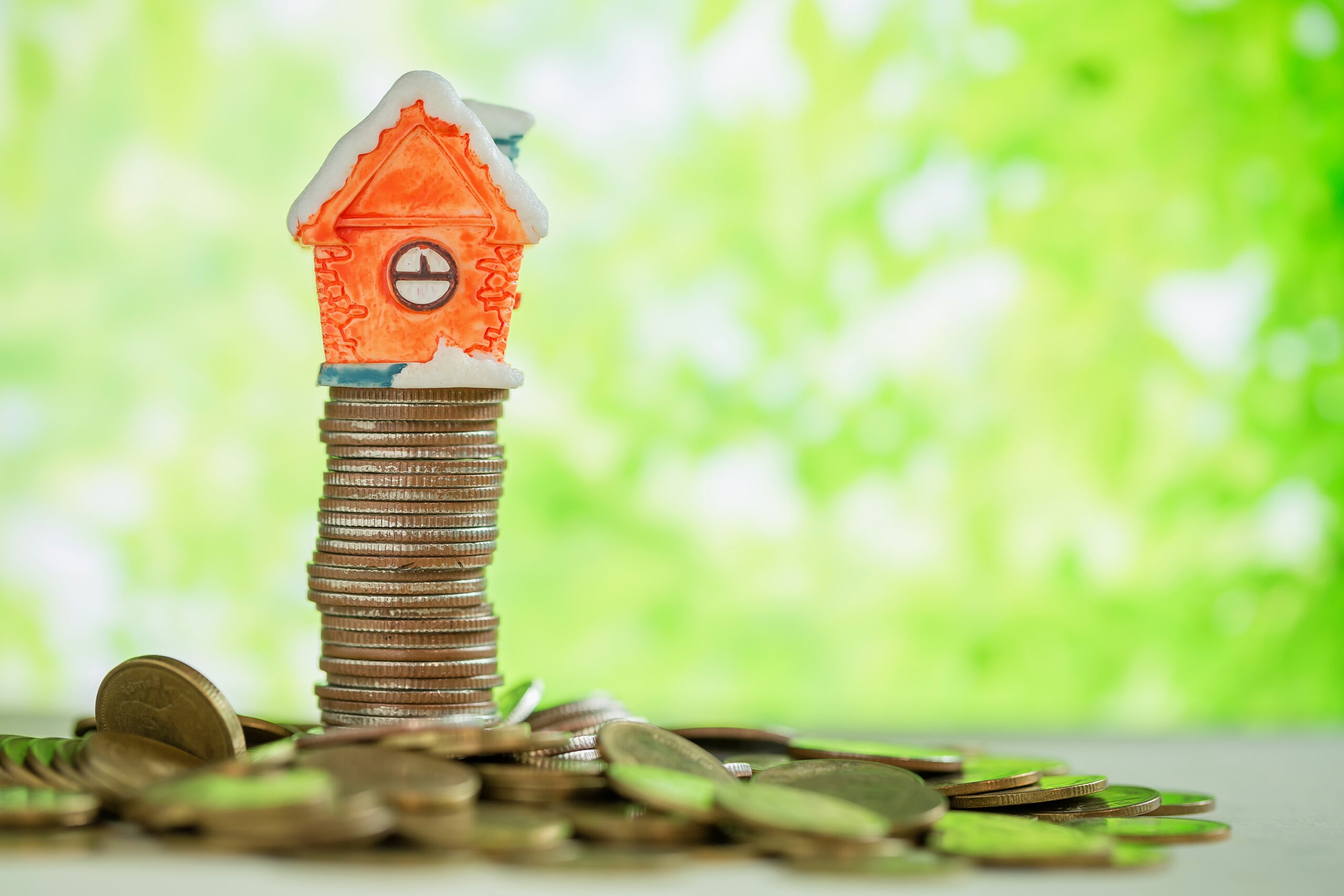 Investment property concept. Mini house on stack of coins with green blur background.